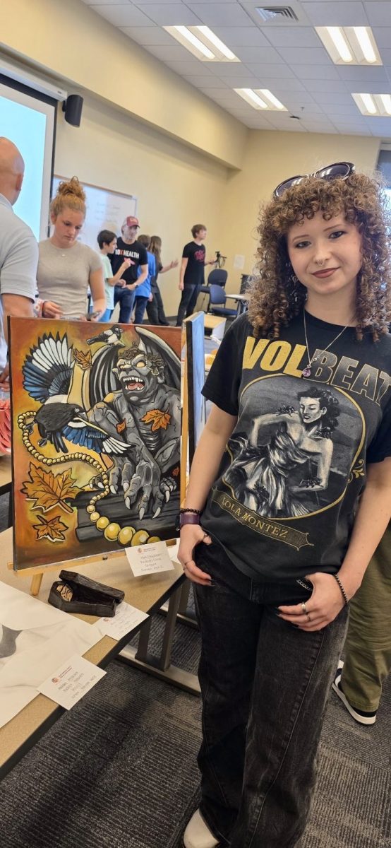 Senior Mya Newnum, whose work is featured in the show, explores both emotional and imaginative themes through her art. Above, she poses with one of pieces.
